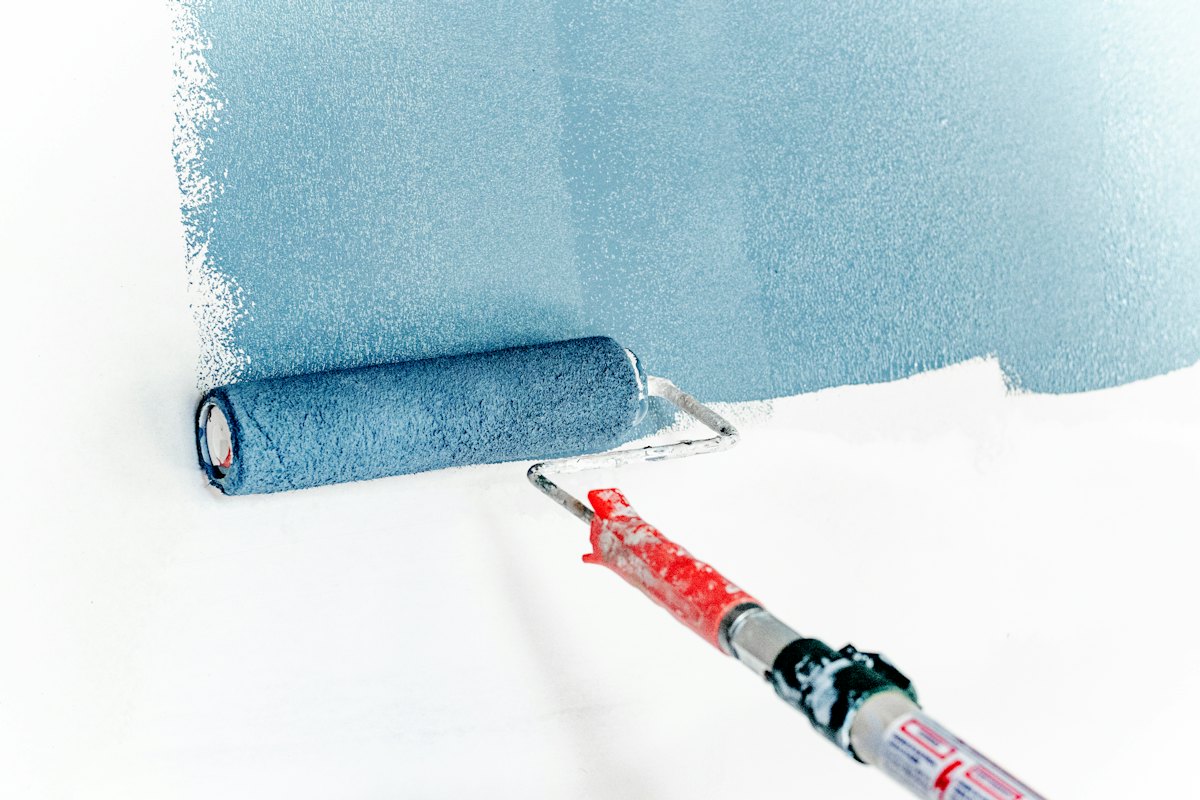 A paint roller putting blue paint on a white wall